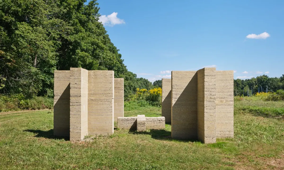Rammed-earth columns forming open passages in a grassy clearing at Art Omi