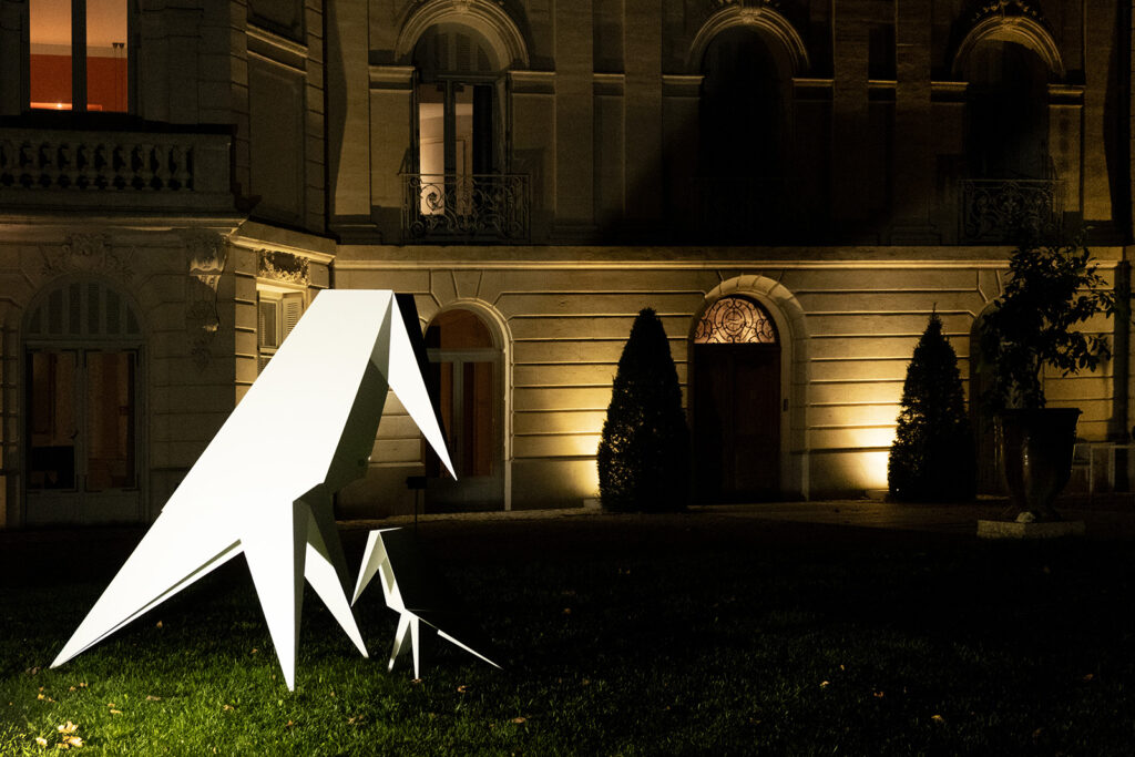 White geometric raven sculptures in front of an illuminated historic façade